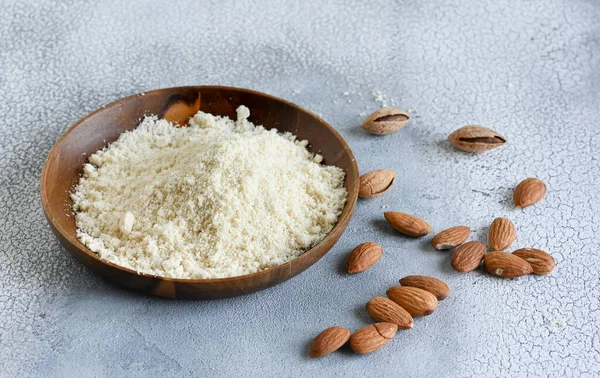 Almond flour in a wooden bowl, almonds on old light background. High quality photo