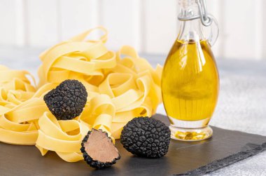 Çiğ İtalyan fettucine makarnası, siyah trüf mantarı ve gri beton arka planda zeytinyağı..
