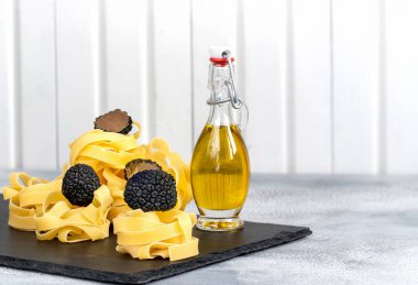Çiğ İtalyan fettucine makarnası, siyah trüf mantarı ve gri beton arka planda zeytinyağı..
