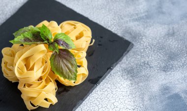 Siyah taş arka planda fesleğenli İtalyan makarna şeklinde rulo tagliatelle. . 