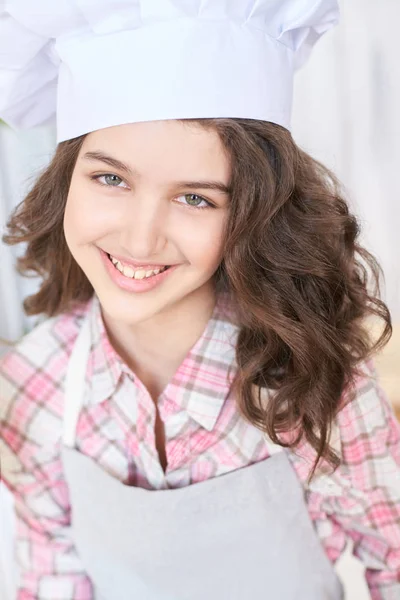 Little cook. Beautiful girl. White cap. Brown curly hair.