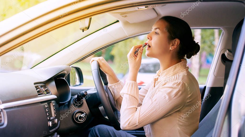 Woman using lipstick inside car. Urban background. Bad busy.