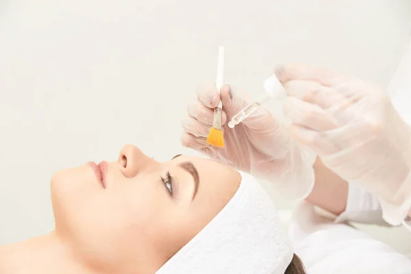 Genç kadın salonda yüz cilt temizliği. Retinol kabuğu fırça ile. Asit organik peeling.