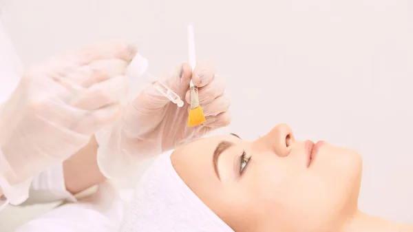 Genç kadın salonda yüz cilt temizliği. Retinol kabuğu fırça ile. Asit organik peeling.