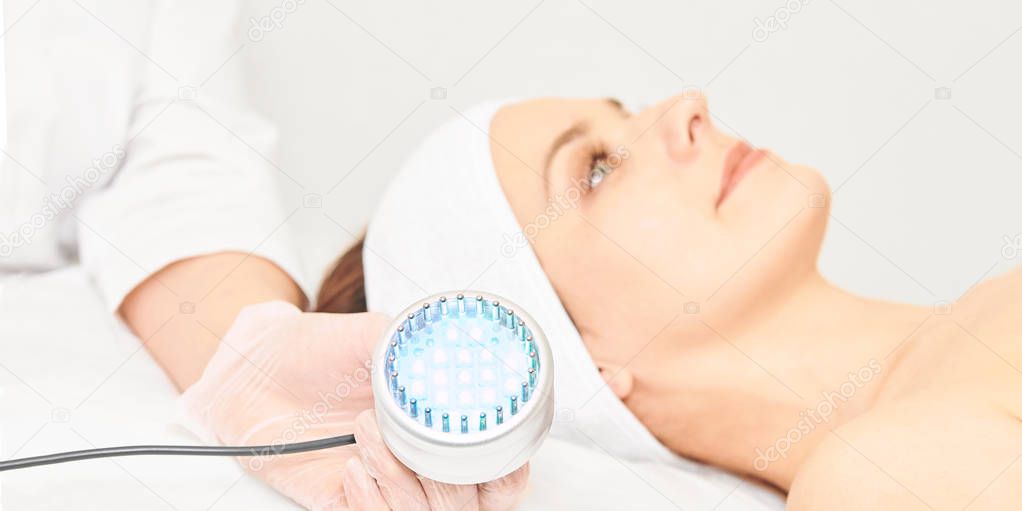 Skincare cosmetology facial procedure. Beauty woman face. Blue light medical therapy. Specialist hand.