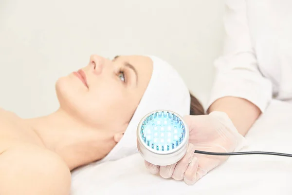 Skincare cosmetology facial procedure. Beauty woman face. Blue light medical therapy. Specialist hand