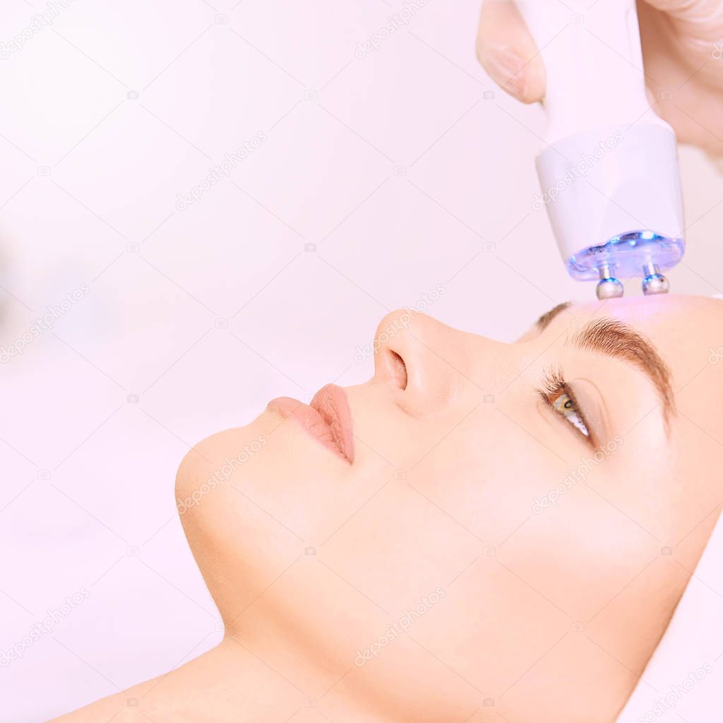 Microcurrent light esthetics procedure. Beauty girl face. Cosmetology machine. Doctor hands. Two micro balls. Wrinkle reduction