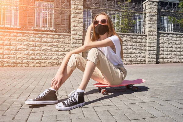 A rapariga sentada no skate. Paisagem urbana. Máscara facial preta reutilizável . — Fotografia de Stock