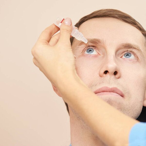 Врач держит глазные капли возле лица пациента