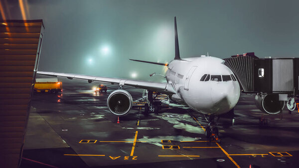 view of aircraft in illuminated foggy airport at night