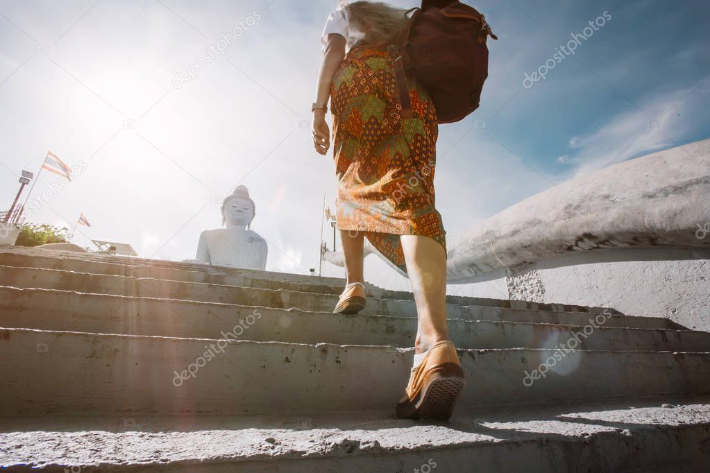 cropped shot of woman traveler walking on stairs with distant Buddha statue