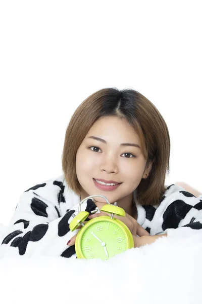 白い背景に分離された緑の目覚まし時計で黒と白のパジャマを着てベッドに横になっている中国の女性 — ストック写真