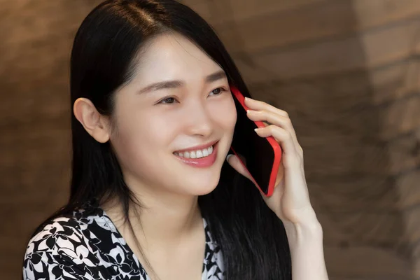 Very happy Chinese American woman using an red smart phone in a coffee shop