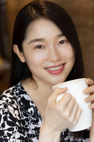 Chinese American woman holding a mug of coffee in a coffee shop with copy space