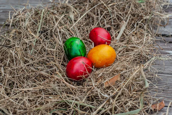 4 colored Easter eggs lays in the dry hay on the wooden aged boa — Stock Photo, Image