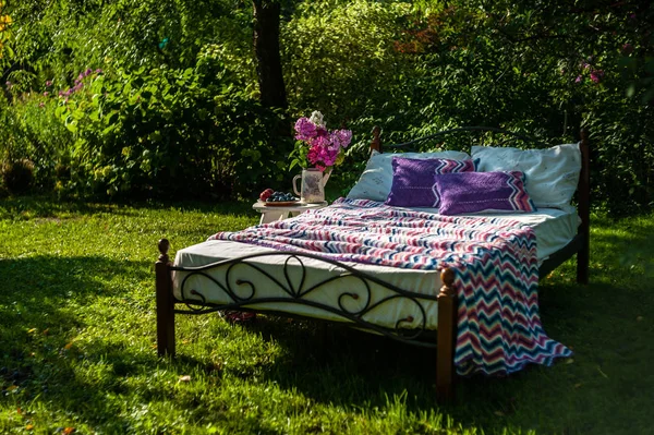 Ein Bett bleibt im grünen Garten, im Freien, mit bunten Blan bedeckt — Stockfoto