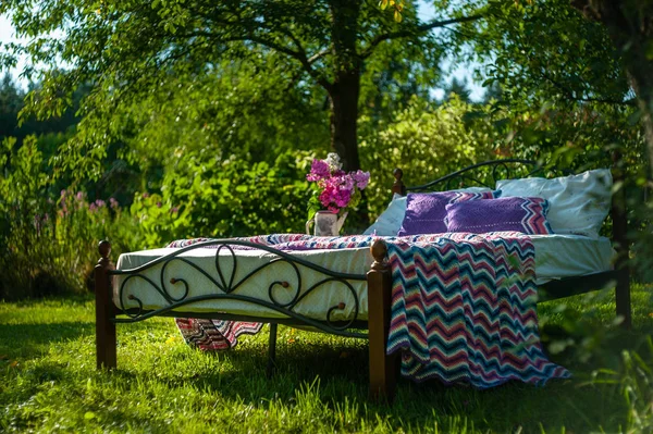 Ein Bett bleibt im grünen Garten, im Freien, mit bunten Blan bedeckt — Stockfoto