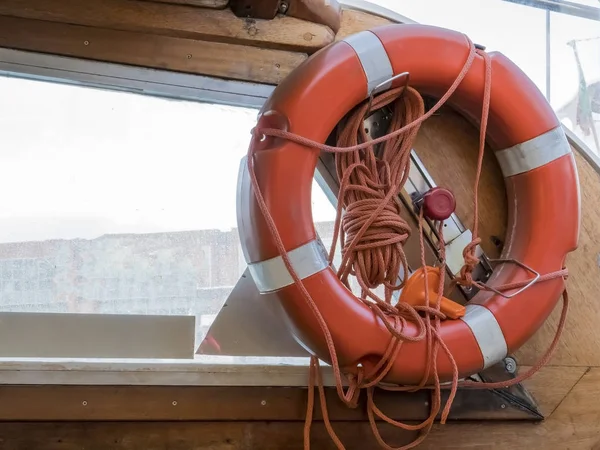 Safe water support aid circle with rope. Rescue red life buoy on wooden background of ship or boat.