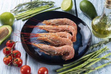 Lagoustine karides, ahşap bir arka planda, sebzelerden oluşan koyu bir tabakta.