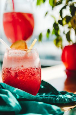 Mavi peçetede pipetle bardakta kırmızı meyve kokteyli.