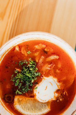 Ekşi limonlu, yuvarlak beyaz bir tabakta çorba ve ahşap bir masada doğranmış otlar.