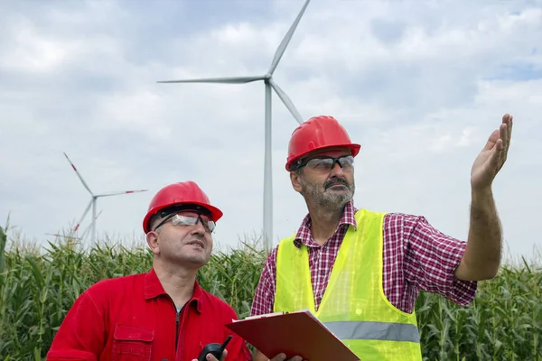 农民们在乡村景观中谈论风力涡轮机 工程师在安全坚硬帽子指向在风力涡轮机 — 图库照片
