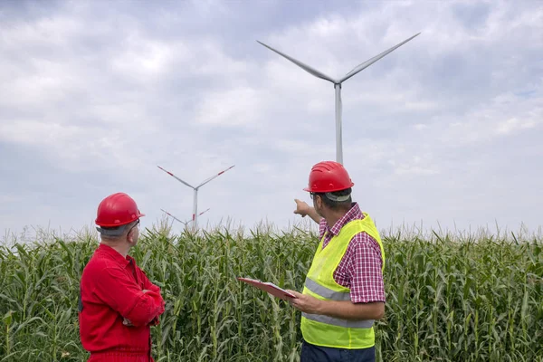 工程师拿着剪贴板站在风电场的同事 乡村景观中的风力涡轮机工人谈话 — 图库照片
