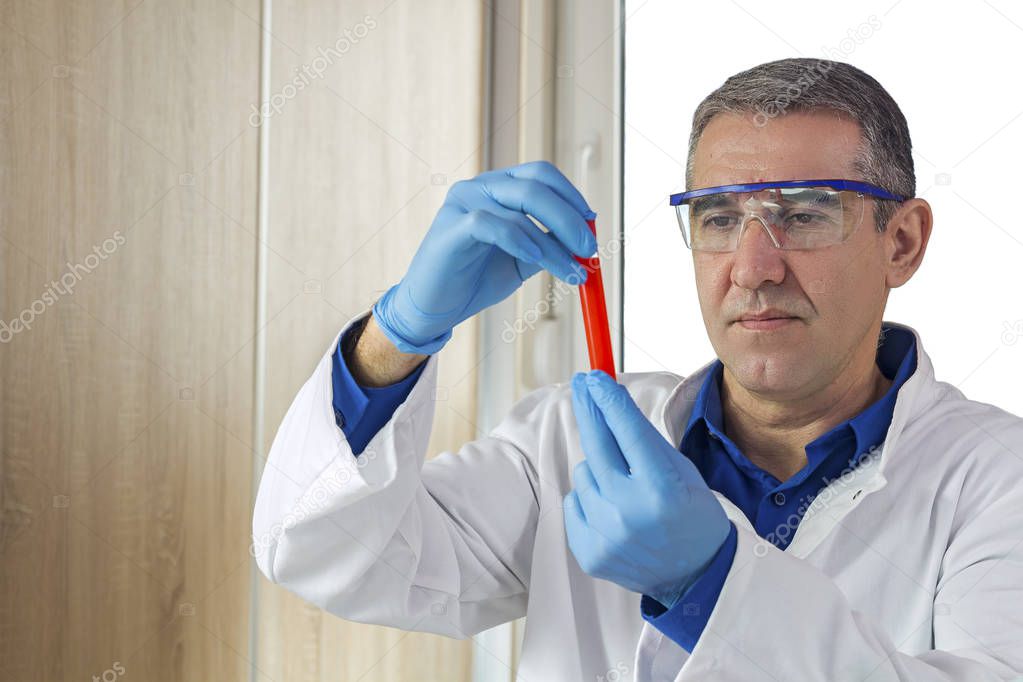 Lab Technician Holding a Blood Sample in a Test Tube. Researcher wearing blue protective gloves, white uniform and safety glasses. 