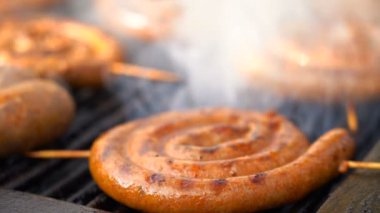 Barbekü Izgara ağır çekimde lezzetli sosis ızgara. Elinde tutan sosis maşa. Yakın çekim görünümü gurme sulu et pişirme ızgara.