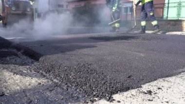 Yapıların işçilerin yolu inşaatı - yavaş hareket üzerinde çalışma. Buhar Rising From sıcak asfalt yüzeydir. A yol inşaatı sitede taze asfalt tesviye işçisi.