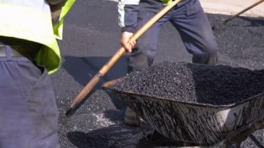 Bir el arabası ile sıcak asfalt yol inşaat sahasında doldurmak için kürek kullanarak yol inşaat işçileri.