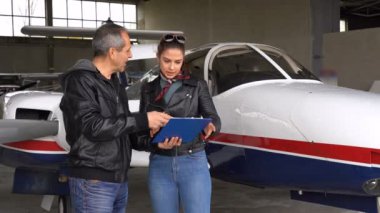 Uçuş Eğitmeni ve Öğrenci Pilotu Hangarda Uçağın Yakınında İmza Lama Belgesi. Genç Kadın Belgeye İmzasını Veriyor. Uçuş Eğitmeni ile Modern Uçak Tarafından Ayakta Güzel Kadın Pilot.
