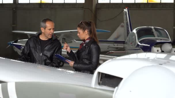 フライトインストラクターと学生パイロットが飛行機の目視検査を行います パイロットによる目視検査または飛行前チェック 空港格納庫の男性と女性のパイロット — ストック動画