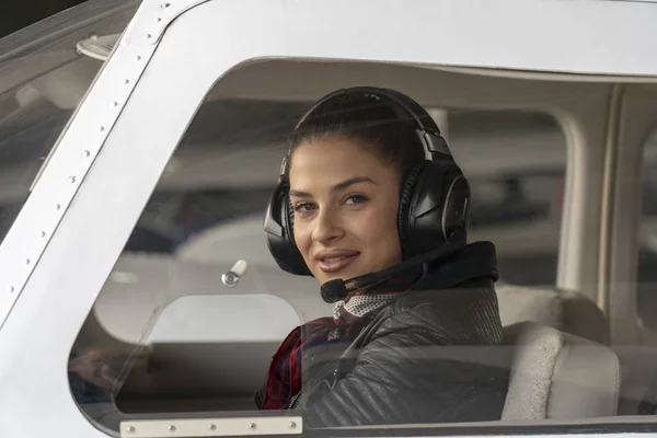 Mladá žena pilot s sluchátky pohledu přes kokpit okno — Stock fotografie