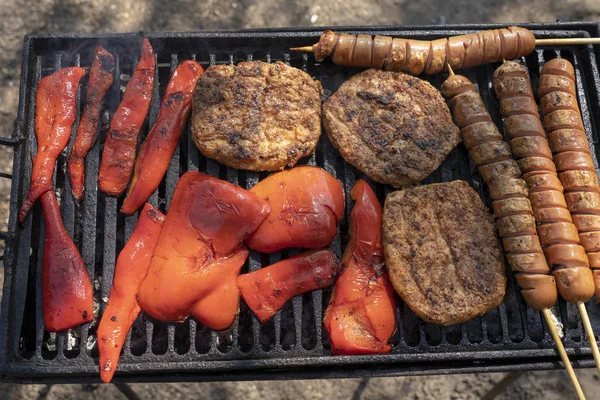 Hamburguesas a la parrilla, salchichas para perros calientes y pimientos rojos en una parrilla de barbacoa — Foto de Stock