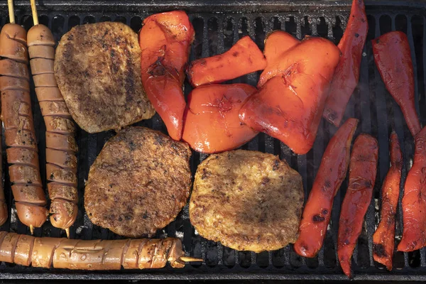 Carne grelhada variada e pimentas vermelhas sobre o carvão em um churrasco — Fotografia de Stock