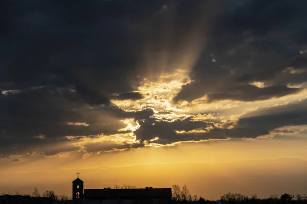 Rayos de sol rompen a través de las nubes sobre la iglesia de la silueta en la noche — Foto de Stock