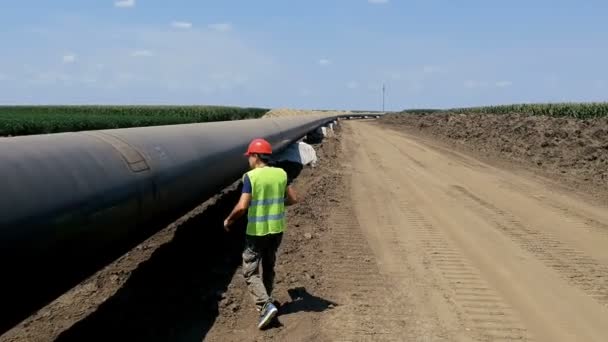 石油パイプラインの隣を歩く労働者 空中ドローン追跡ショット 建設現場で石油化学石油 ガスパイプラインをチェックするエンジニア 建設中のパイプライン — ストック動画