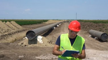 Gaz Boru Hattı Şantiyesi'nde Panoüzerine Mühendis Yazısı. Borular destekleyici kum torbaları üzerine serilir, birlikte kaynaklı ve epoks ile kaplanmış kaynak eklemleri. Boru hattı yapım aşamasında.