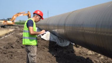 İnşaat Sahasında Petrokimyasal Gaz Boru Hattı Mühendisi Kontrol. Pano ve Radyo İletişim Cihazı ile Kırmızı Sert Şapka ve Sarı Yelek li Bir İşçinin Portresi. Boru Hattı Yapım Aşamasında.