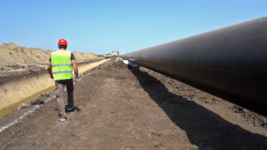 Gaz Boru Hattı Şantiyesinde Yavaş Çekimde Yürüyen Kırmızı Kasklı Mühendis. Boru Hattı Yapım Aşamasında. Mühendis Kontrol Petrokimya Petrol / Gaz Boru Hattı.