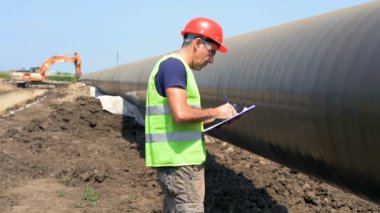 Gaz Boru Hattı Şantiyesinde Yavaş Hareket Panosuna Mühendis Yazımı. Elinde Pano ile Kırmızı Sert Şapka ve Sarı Yelek bir Süpervizör Portresi. Boru Hattı Yapım Aşamasında.