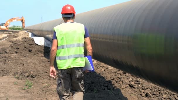 石油パイプライン建設現場をスローモーションで歩くエンジニア 建設現場で石油化学石油 ガスパイプラインをチェックするエンジニア 建設中のパイプライン — ストック動画