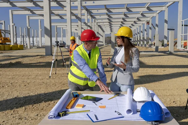 Volwassen ingenieur en vrouwelijke architect controleren van de blauwdruk van de bouw op bouwplaats — Stockfoto