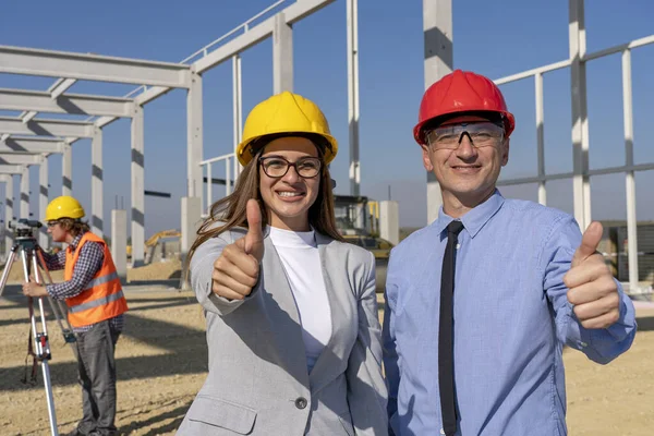 Glimlachende vrouwelijke architect en volwassen zakenman met duimen op een bouwplaats — Stockfoto