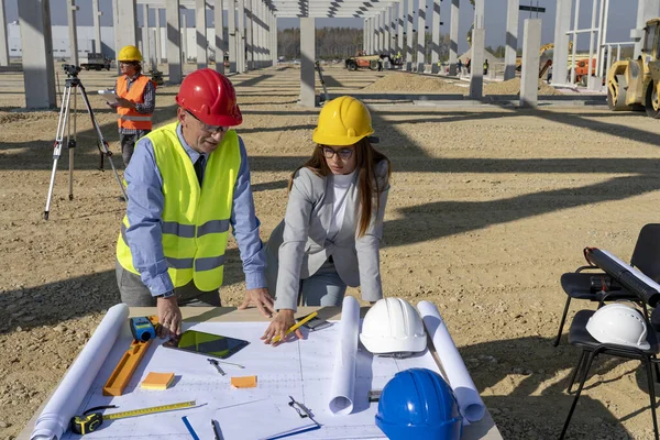 Hombre de negocios maduro y arquitecta joven que planea un proyecto de construcción en el sitio de construcción — Foto de Stock