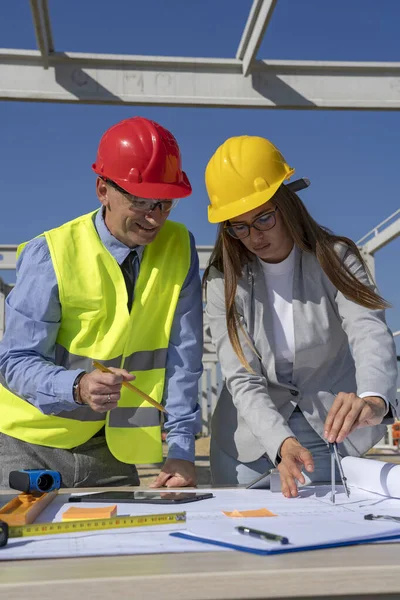 Lachende volwassen zakenman en jonge vrouwelijke architecten bouwproject op bouwplaats — Stockfoto