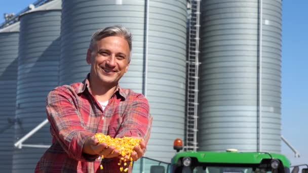 农民在粮仓上展示新鲜收获的玉米和玉米谷物 农民手里拿着玉米核看着相机 用新的玉米收获对农民施肥 — 图库视频影像
