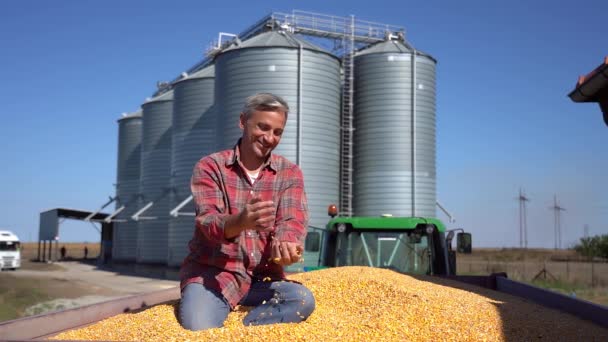 Uśmiechnięty Farmer Siedzi Przyczepie Ciągnika Pełna Nasion Kukurydzy Przed Kosze — Wideo stockowe