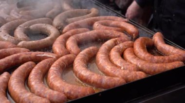 Yemek standında Sosis Pişiren Sokak Satıcısı. Açık Mutfakta İştah açıcı Barbekü Sosisleri Pişiyor. Lezzetli Sosisler Büyük Ticari Izgara Fırınında.